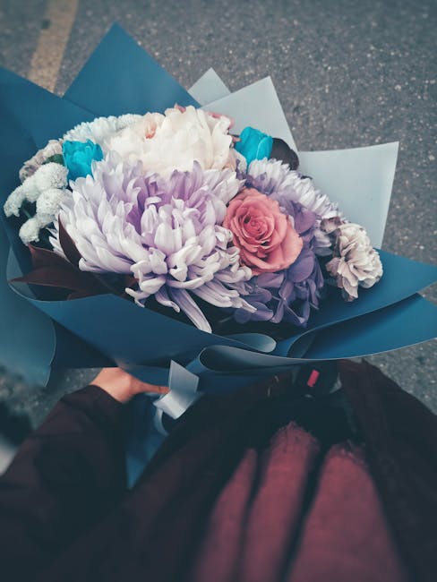 A vibrant floral bouquet featuring a mix of fresh flowers arranged in a harmonious composition. The bouquet includes a large, soft white chrysanthemum, pink roses with tightly layered petals, and purp